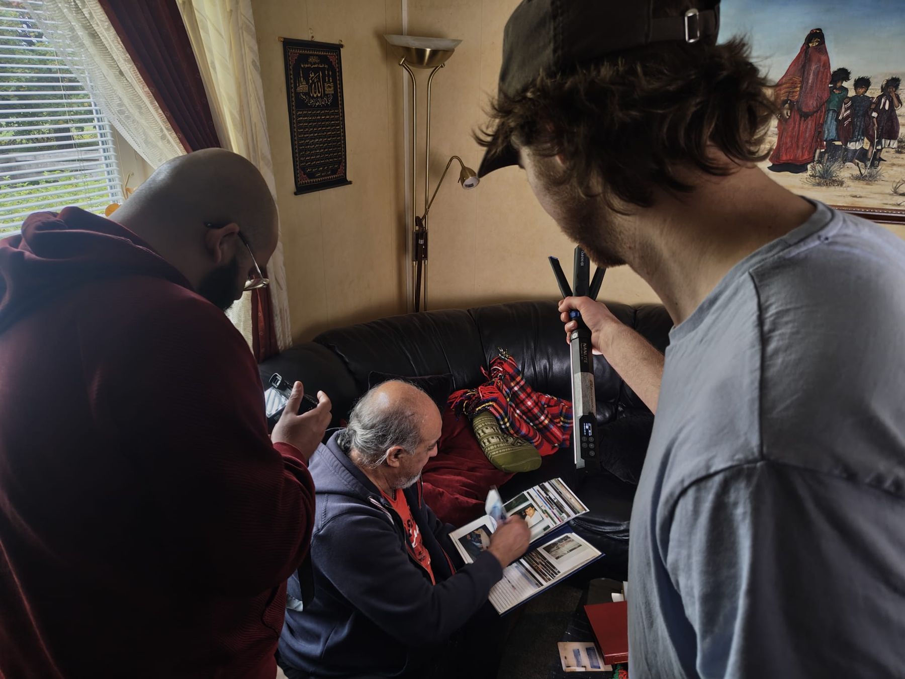 The crew lighting Walid with a tube light while he looks through a photo album