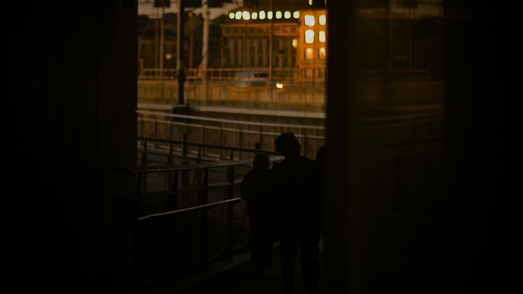 Silhouettes on a bridge against warm city lights at night