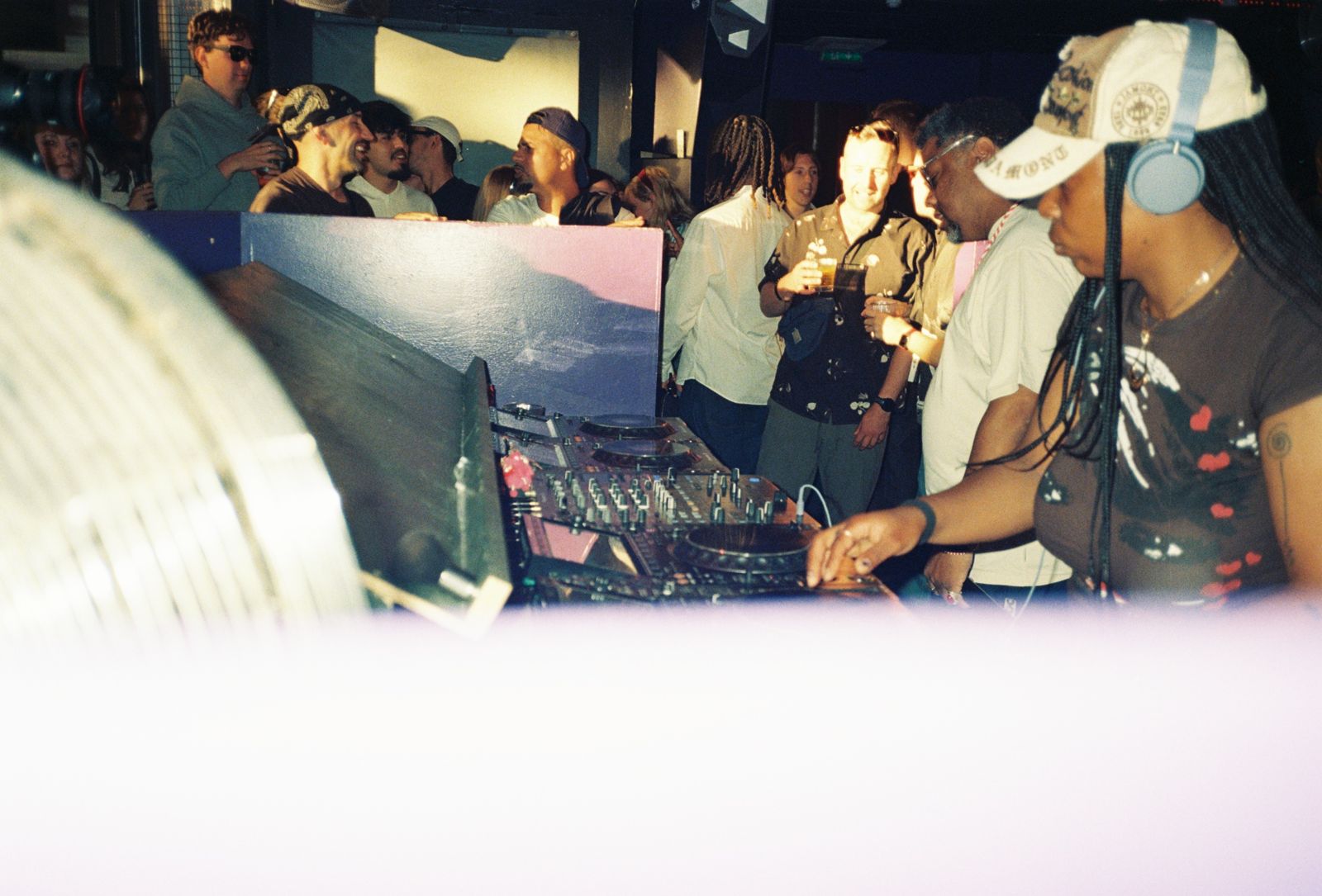 A DJ at the decks in warm light, crowd behind