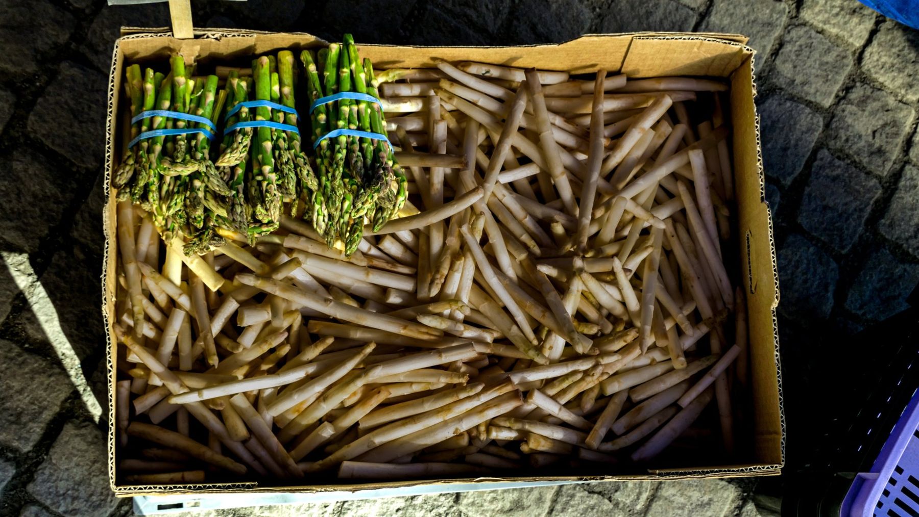 A cardboard box of white asparagus with green bundles on top